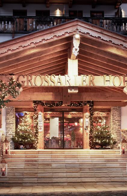 Festlich dekorierter Hoteleingang mit Holzverkleidung und weihnachtlicher Beleuchtung, geschmückt mit Tannenbäumen und Schriftzug. | © Michael Huber I www.huber-fotografie.at