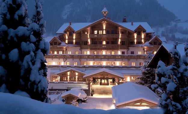 Winterliche Außenansicht des Boutique Hotel Salzburg bei Nacht, stimmungsvoll beleuchtet und umgeben von verschneiter Berglandschaft | © Michael Huber I www.huber-fotografie.at