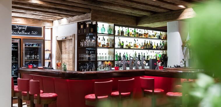 Stilvolle Bar im Boutique Hotel Salzburg mit roter Sitzpolsterung, beleuchteten Regalen und rustikalem Ambiente | © www.fabianfranzferdinand.com