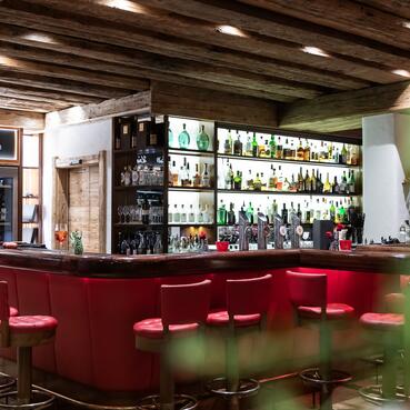 Stilvolle Bar im Boutique Hotel Salzburg mit roter Sitzpolsterung, beleuchteten Regalen und rustikalem Ambiente | © www.fabianfranzferdinand.com