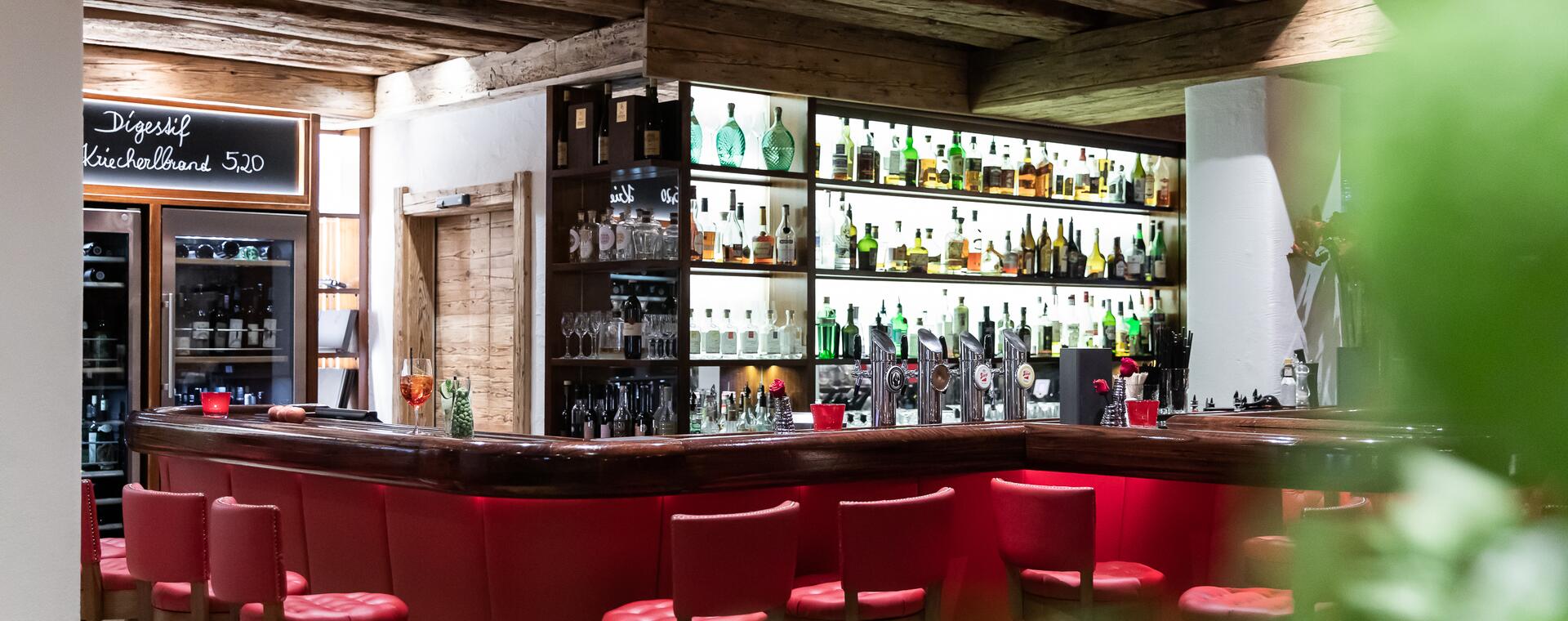 Stilvolle Bar im Boutique Hotel Salzburg mit roter Sitzpolsterung, beleuchteten Regalen und rustikalem Ambiente | © www.fabianfranzferdinand.com