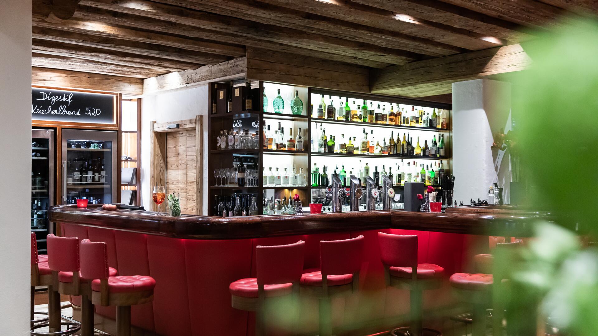 Stilvolle Bar im Boutique Hotel Salzburg mit roter Sitzpolsterung, beleuchteten Regalen und rustikalem Ambiente | © www.fabianfranzferdinand.com