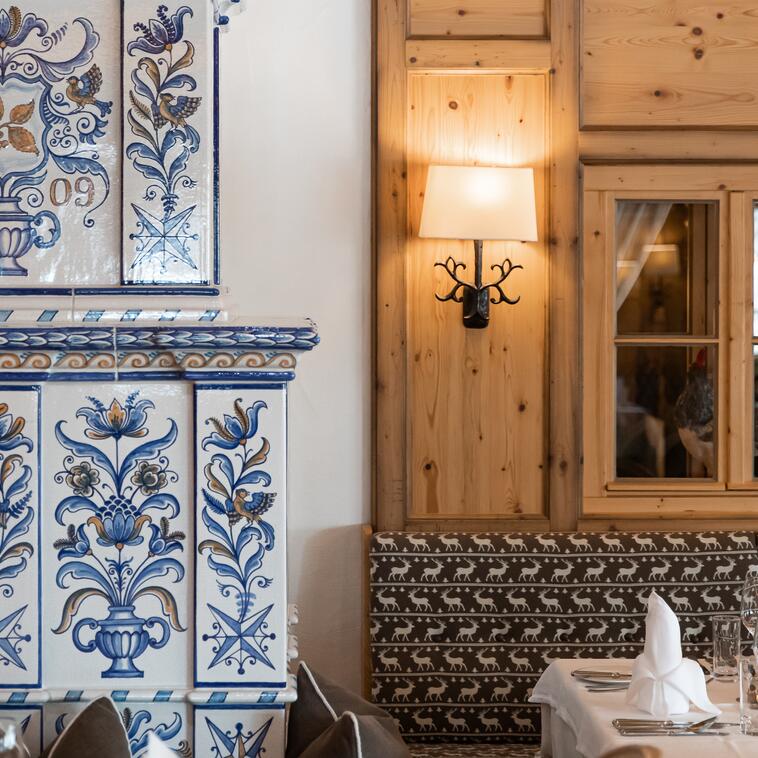 Detail eines kunstvoll verzierten Kachelofens im Boutique Hotel Salzburg, kombiniert mit traditioneller Holzwand und stilvoller Beleuchtung