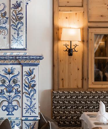Detail eines kunstvoll verzierten Kachelofens im Boutique Hotel Salzburg, kombiniert mit traditioneller Holzwand und stilvoller Beleuchtung