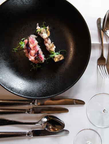 Gourmet-Vorspeise auf schwarzem Teller, dekoriert mit essbarem Blattgold, kunstvoll angerichtet und auf elegant gedecktem Tisch serviert