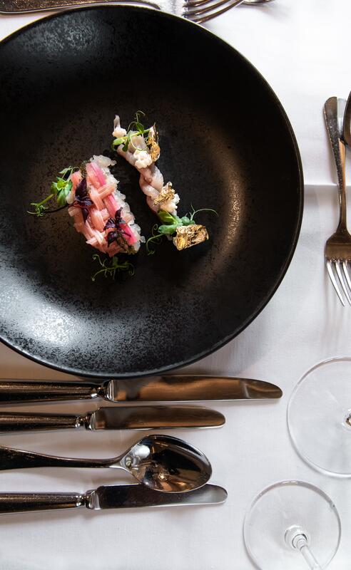 Gourmet-Vorspeise auf schwarzem Teller, dekoriert mit essbarem Blattgold, kunstvoll angerichtet und auf elegant gedecktem Tisch serviert