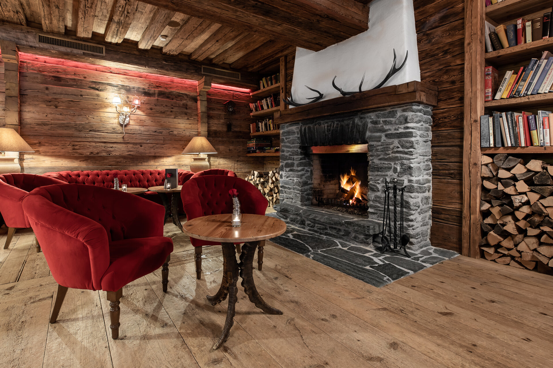 Gemütliche Lounge im Boutique Hotel Salzburg mit knisterndem Kamin, roten Sesseln und rustikaler Holzeinrichtung für entspannte Abende