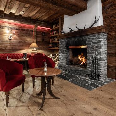 Gemütliche Lounge im Boutique Hotel Salzburg mit knisterndem Kamin, roten Sesseln und rustikaler Holzeinrichtung für entspannte Abende