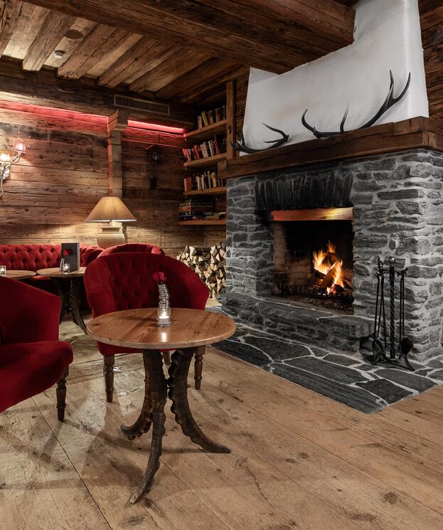 Gemütliche Lounge im Boutique Hotel Salzburg mit knisterndem Kamin, roten Sesseln und rustikaler Holzeinrichtung für entspannte Abende | © SPORTALPEN