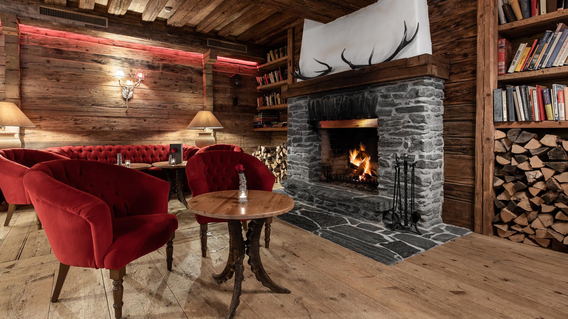 Gemütliche Lounge im Boutique Hotel Salzburg mit knisterndem Kamin, roten Sesseln und rustikaler Holzeinrichtung für entspannte Abende