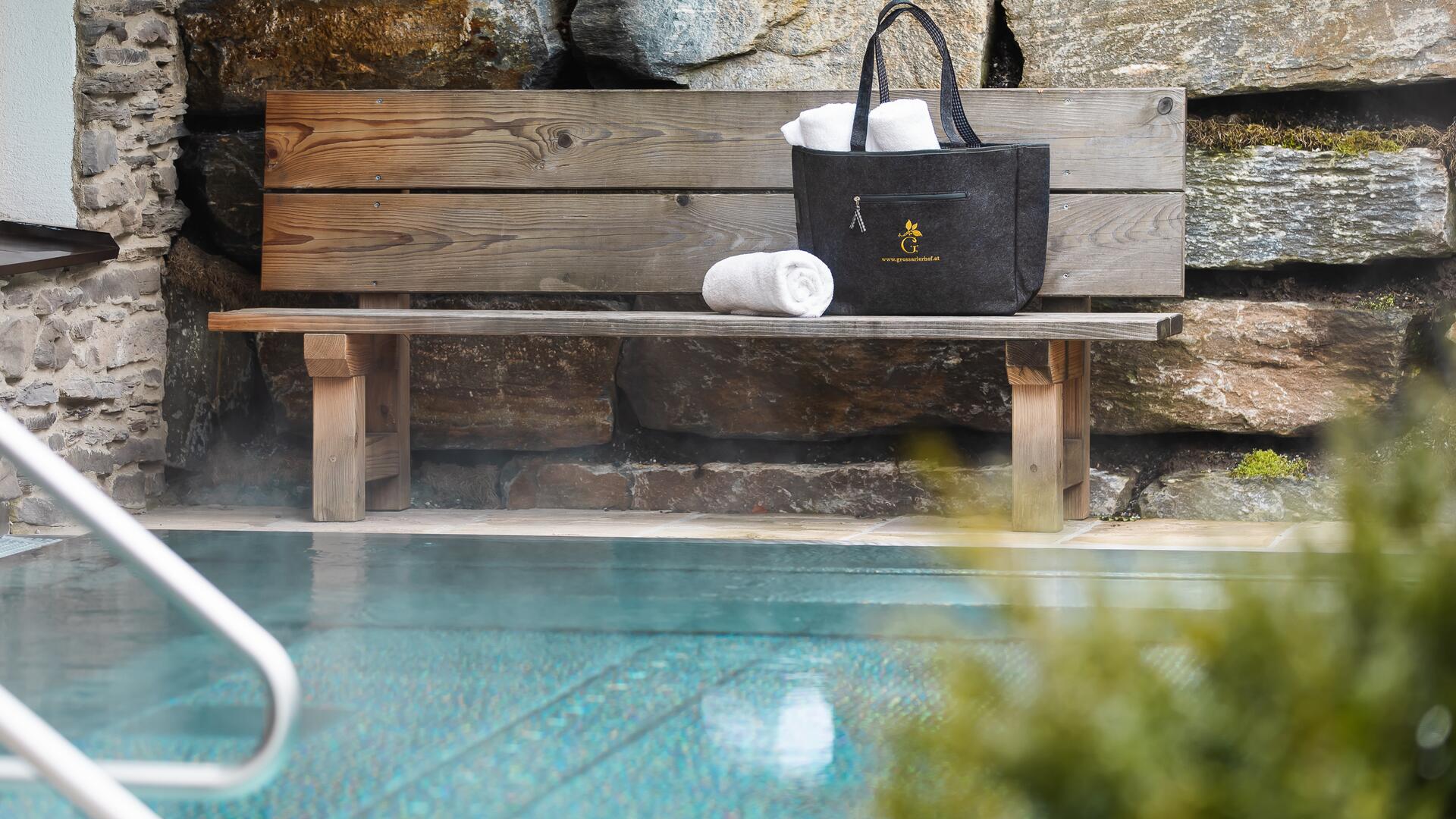 Entspannender Poolbereich im Boutique Hotel Salzburg mit Holzbank, Handtüchern und eleganter Tasche für einen erholsamen Aufenthalt | © SPORTALPEN