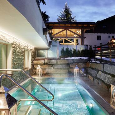 Beleuchteter Außenpool in winterlicher Umgebung, umgeben von Steinmauern, Laternen und einem gemütlichen Hotelambiente in der Dämmerung | © Michael Huber I www.huber-fotografie.at