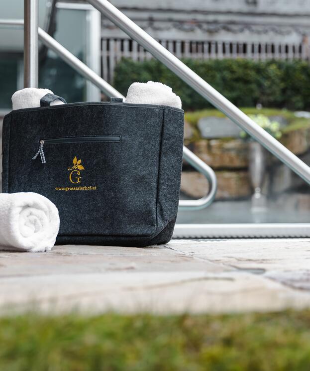 Schwarze Tasche mit Handtüchern, ein Handtuch liegt auf dem Boden. Perfekt für eine Auszeit im Salzburger Land.