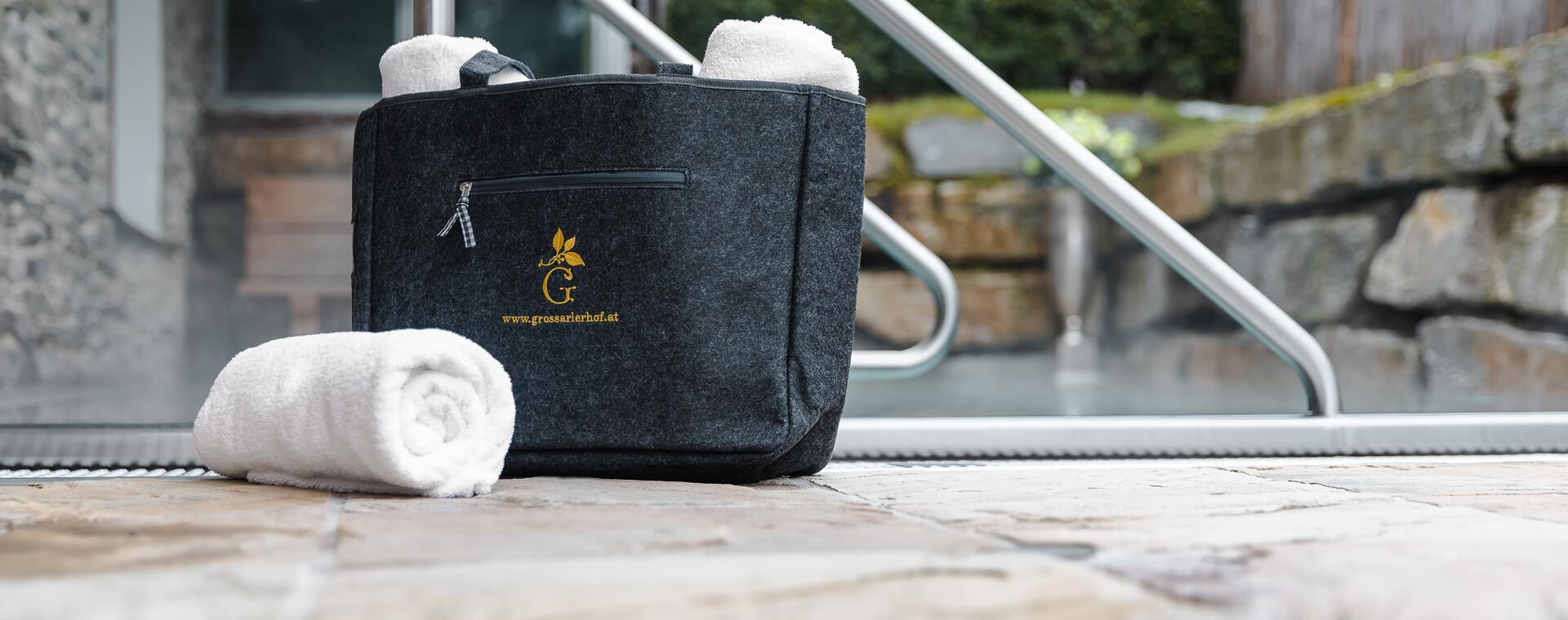Schwarze Tasche mit Handtüchern, ein Handtuch liegt auf dem Boden. Perfekt für eine Auszeit im Salzburger Land.