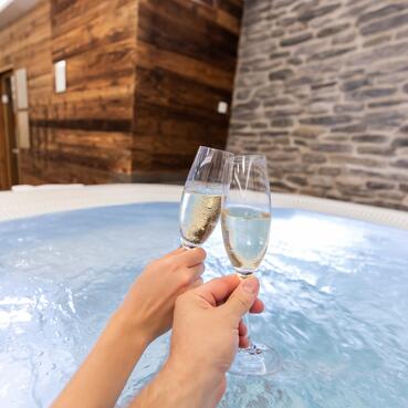 Zwei Menschen stoßen mit Champagner im Whirlpool an und genießen eine Auszeit im Salzburger Land