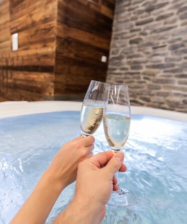 Zwei Menschen stoßen mit Champagner im Whirlpool an und genießen eine Auszeit im Salzburger Land