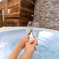 Zwei Menschen stoßen mit Champagner im Whirlpool an und genießen eine Auszeit im Salzburger Land