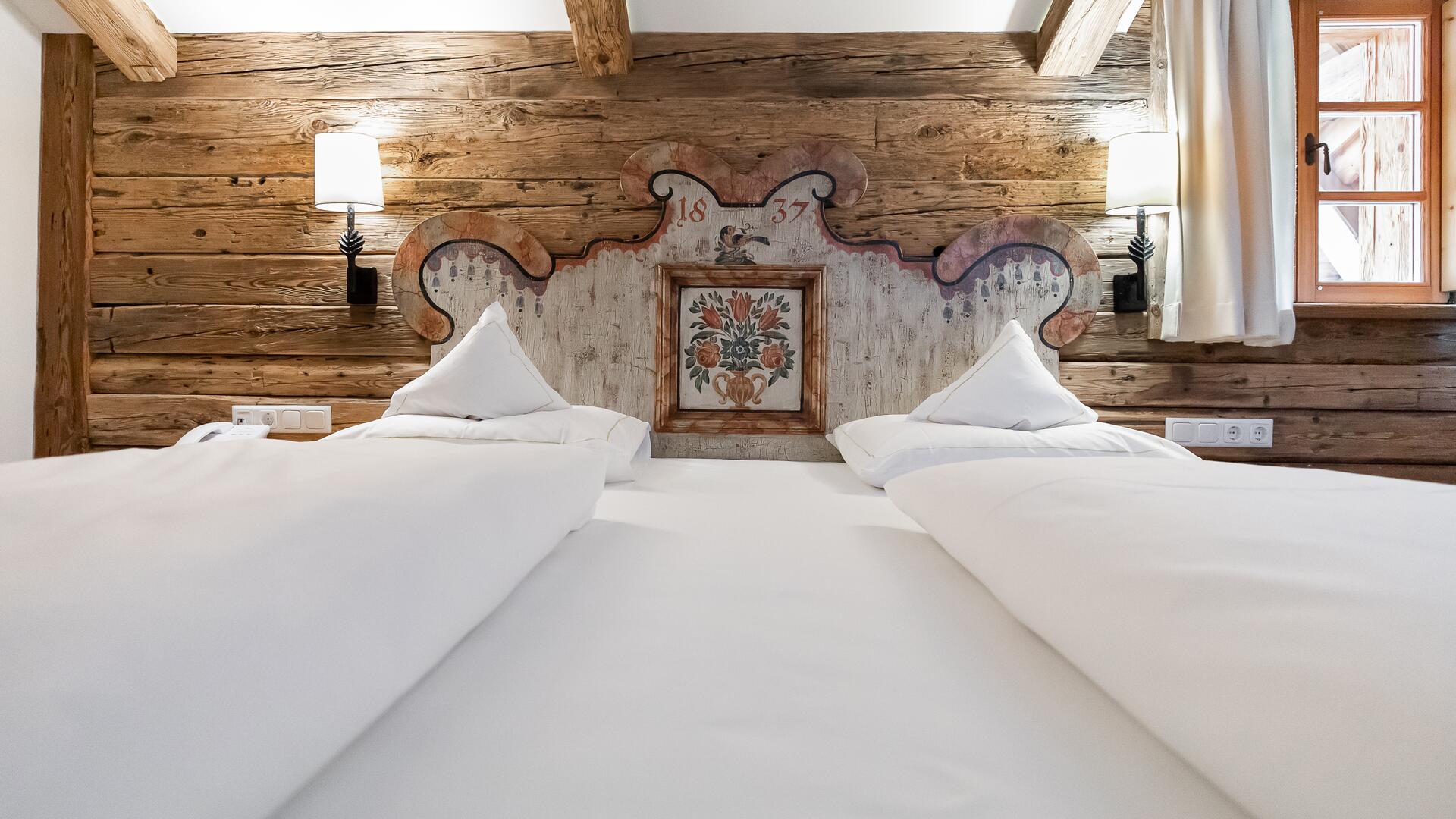 Gemütliches Zimmer im Boutique Hotel Salzburg mit rustikaler Holzverkleidung, kunstvollem Kopfteil und traditionellem Charme für erholsame Nächte