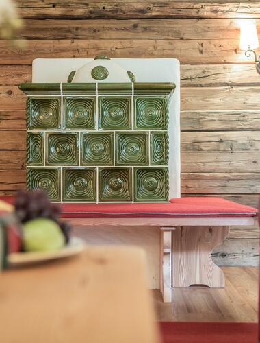 Traditioneller grüner Kachelofen mit Sitzbank im Boutique Hotel Salzburg, ergänzt durch rustikale Holzelemente und gemütliches Ambiente