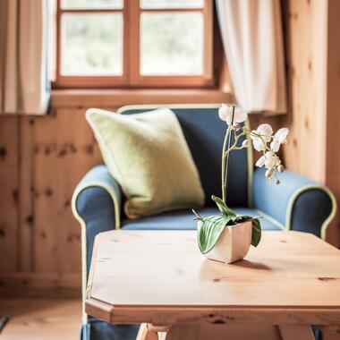 Detailansicht eines Zimmers im Boutique Hotel Salzburg mit blauem Sessel, grüner Kissen und dekorativer Orchidee auf einem Holztisch