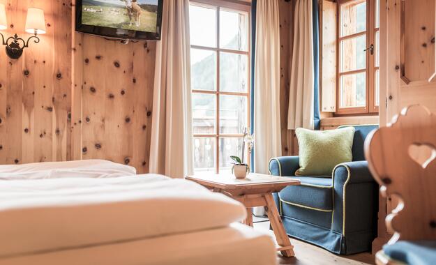 Gemütliches Zimmer im Boutique Hotel Salzburg mit Holzwänden, blauem Sessel, Balkonblick und einladendem Ambiente