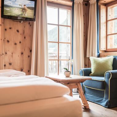 Gemütliches Zimmer im Boutique Hotel Salzburg mit Holzwänden, blauem Sessel, Balkonblick und einladendem Ambiente