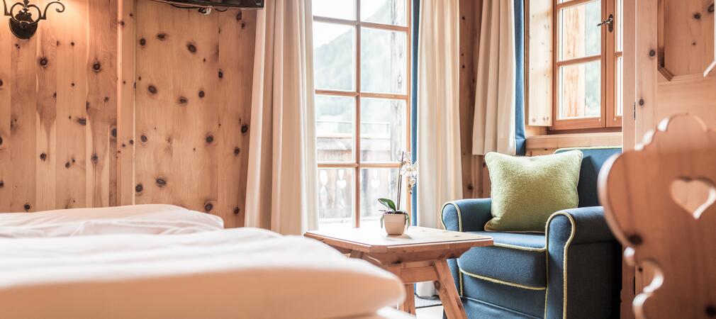 Gemütliches Zimmer im Boutique Hotel Salzburg mit Holzwänden, blauem Sessel, Balkonblick und einladendem Ambiente