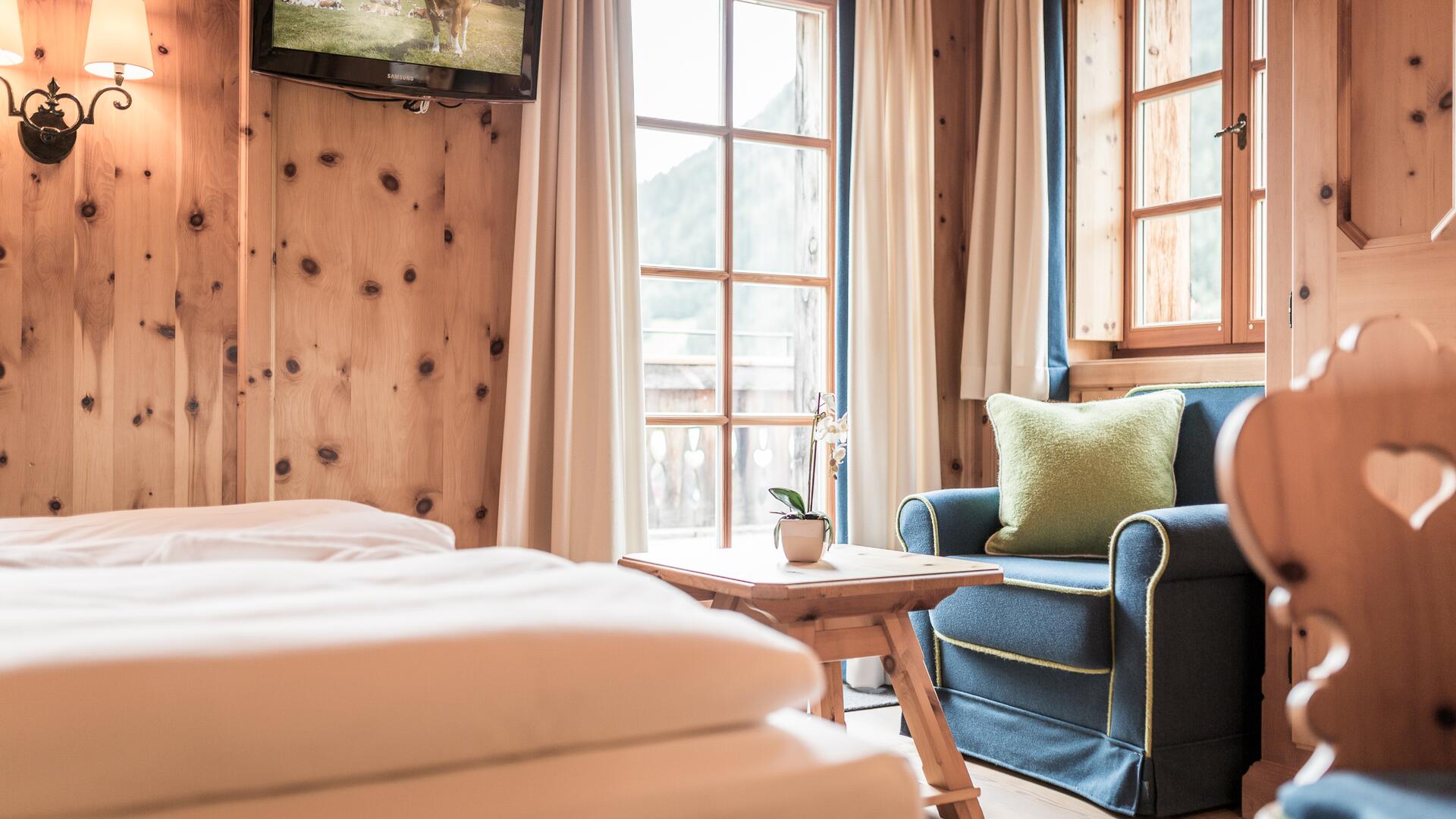 Gemütliches Zimmer im Boutique Hotel Salzburg mit Holzwänden, blauem Sessel, Balkonblick und einladendem Ambiente