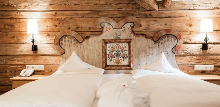 Gemütliches Doppelbett im Boutique Hotel Salzburg mit kunstvollem, traditionellem Holzkopfteil und rustikalem Charme
