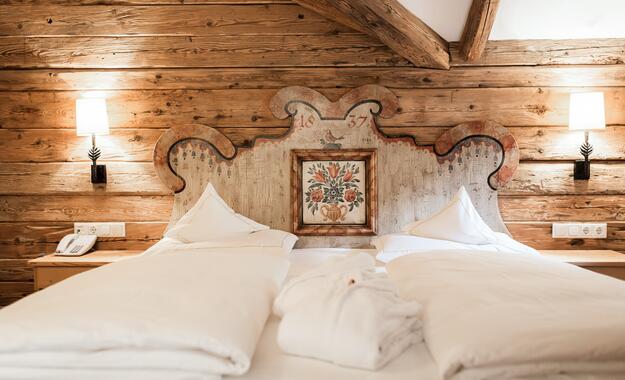 Gemütliches Doppelbett im Boutique Hotel Salzburg mit kunstvollem, traditionellem Holzkopfteil und rustikalem Charme