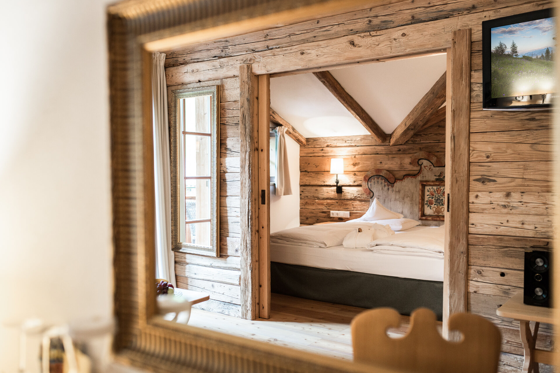 Spiegelblick auf ein rustikales Zimmer im Boutique Hotel Salzburg mit Holzwänden, sichtbaren Balken und gemütlichem Doppelbett