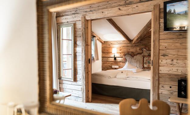 Spiegelblick auf ein rustikales Zimmer im Boutique Hotel Salzburg mit Holzwänden, sichtbaren Balken und gemütlichem Doppelbett