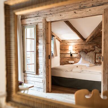Spiegelblick auf ein rustikales Zimmer im Boutique Hotel Salzburg mit Holzwänden, sichtbaren Balken und gemütlichem Doppelbett