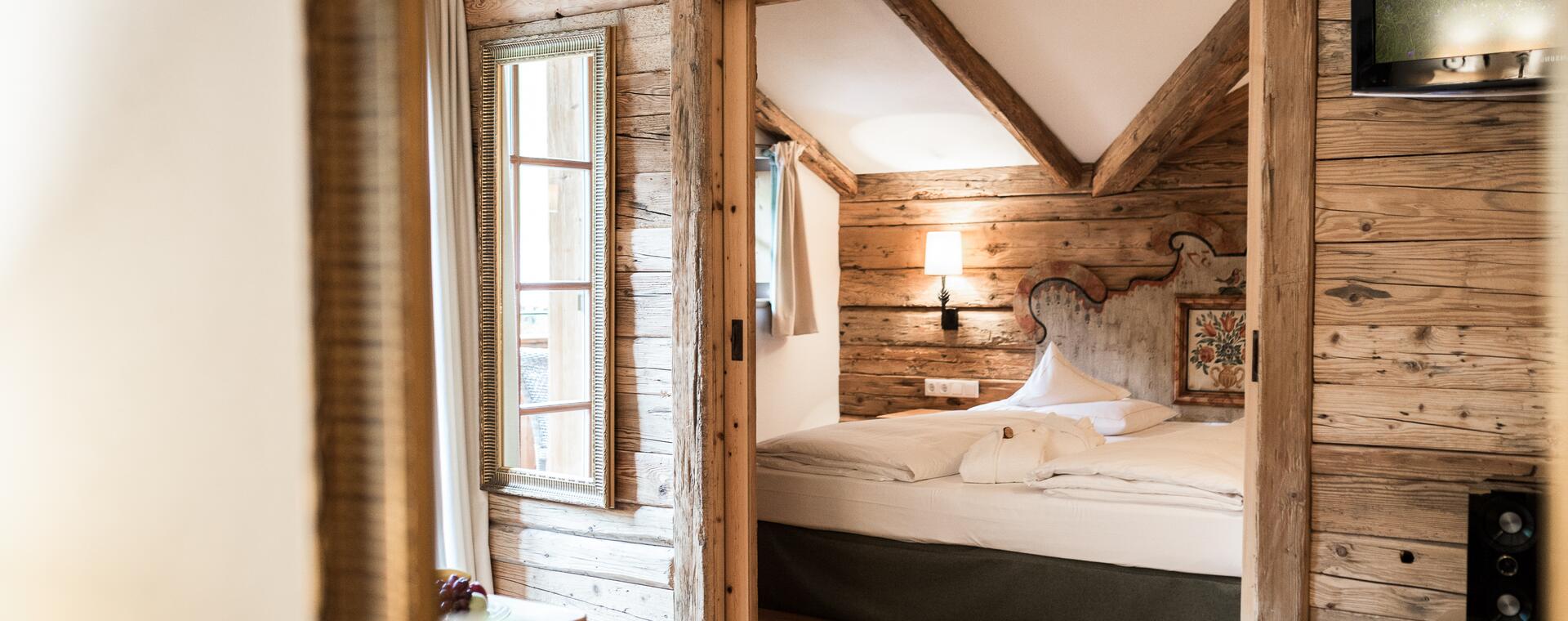 Spiegelblick auf ein rustikales Zimmer im Boutique Hotel Salzburg mit Holzwänden, sichtbaren Balken und gemütlichem Doppelbett