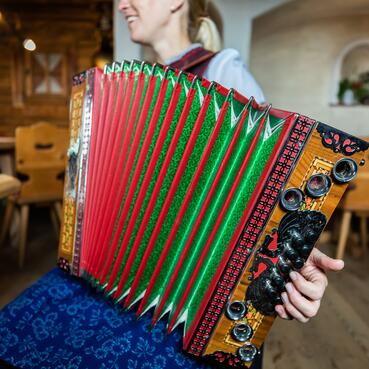 Eine Frau trägt traditionelle Kleidung und spielt Akkordeon in einer Alm im Salzburger Land.