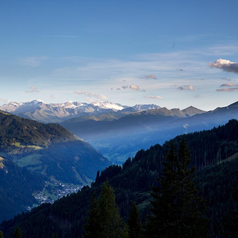 Blick von der Berghütte im Salzburger Land auf majestätische Berge und grüne Bäume in der Umgebung. | © Michael Huber I www.huber-fotografie.at