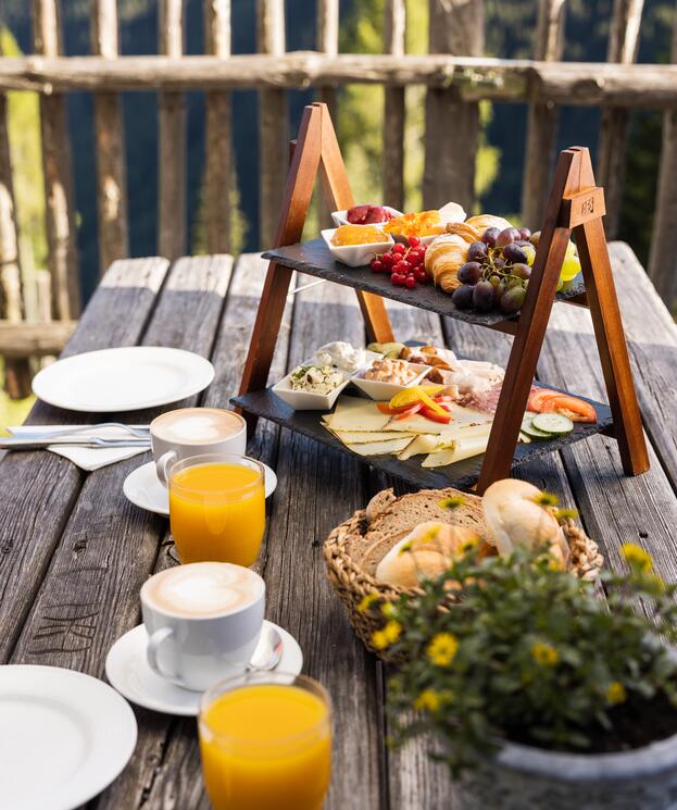 Rustikales Frühstück im Boutique Hotel Salzburg mit regionalen Spezialitäten, frischem Gebäck und Säften, auf einer Holzterrasse mit Bergblick