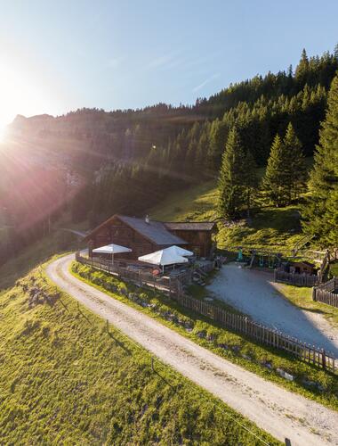 Idyllische Almhütte nahe dem Boutique Hotel Salzburg bei Sonnenaufgang, umgeben von malerischer Berglandschaft und grünen Wiesen