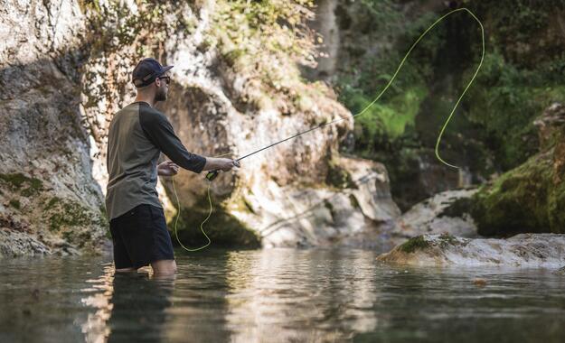 Mann steht im Wasser und wirft Angelrute aus | © Michael Groessinger