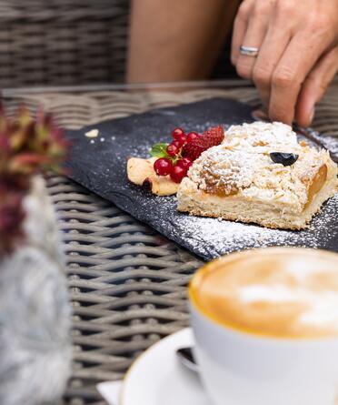 Genussmoment im Boutique Hotel Salzburg: Hausgemachter Kuchen mit frischen Beeren und ein Cappuccino auf einem stilvoll gedeckten Tisch