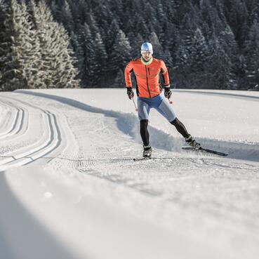 Langläufer auf der Strecke während einer Großarl Skitour, umgeben von verschneiten Bäumen und idyllischer Winterlandschaft