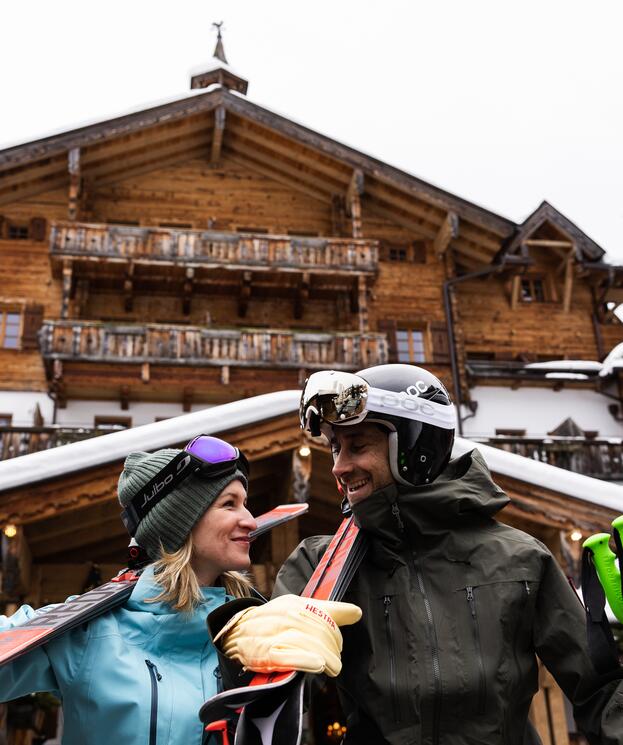 Pärchen mit Skiern vor einem traditionellen Chalet im Salzburger Land, bereit für ihren Skiurlaub im Salzburger Land