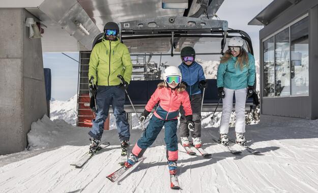 Familie auf Skiern vor einem Sessellift, ausgestattet mit Skianzügen, Helmen und Skibrillen | © SalzburgerLand Tourismus