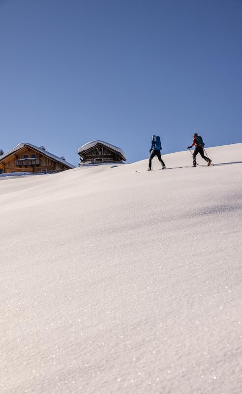 Zwei Wanderer im Schnee mit Sporthotel im Salzburger Land im Hintergrund.