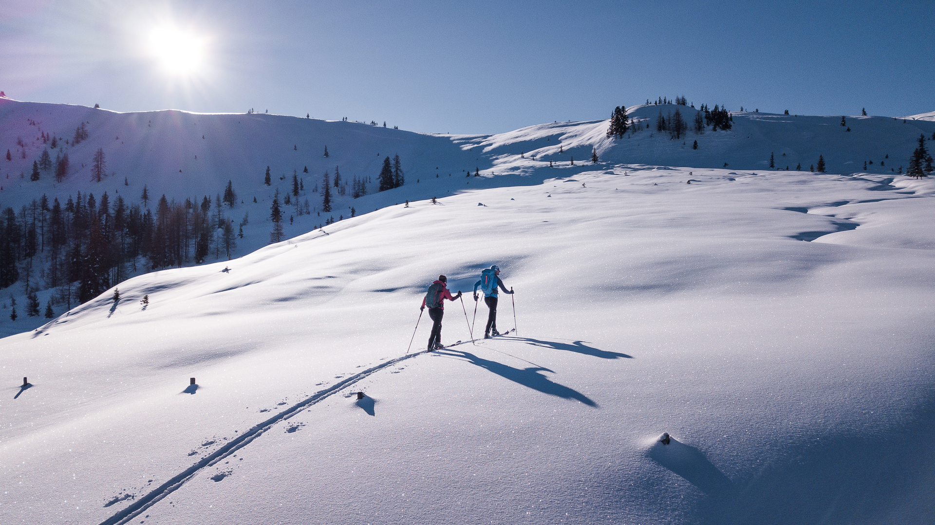 Two ski tourers in a snow-covered mountain landscape on a sunny winter day
