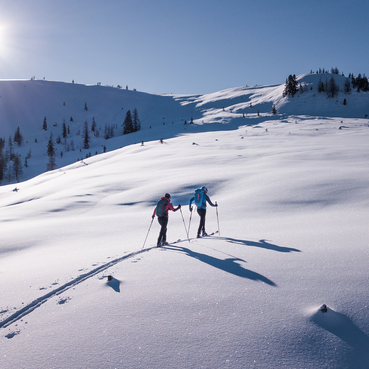 Two ski tourers in a snow-covered mountain landscape on a sunny winter day