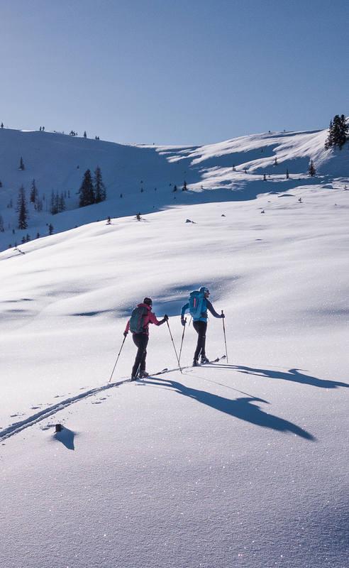 Two ski tourers in a snow-covered mountain landscape on a sunny winter day